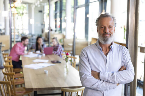 Porträt eines reifen Geschäftsmannes in einem Café mit Kollegen, die im Hintergrund eine Besprechung abhalten, lizenzfreies Stockfoto