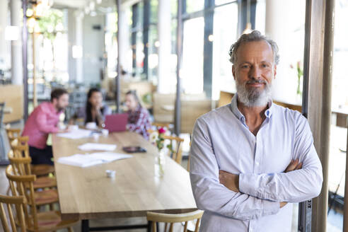 Portrait of mature businessman in a cafe with colleagues having a meeting in background - FKF03673