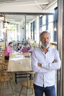 Porträt eines reifen Geschäftsmannes in einem Café mit Kollegen, die im Hintergrund eine Besprechung abhalten - FKF03674