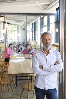 Portrait of mature businessman in a cafe with colleagues having a meeting in background - FKF03674