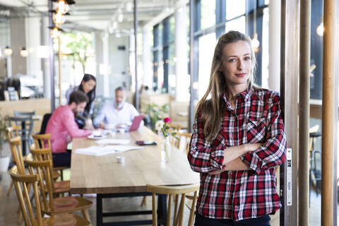 Porträt einer lässigen Geschäftsfrau in einem Café mit Kollegen, die im Hintergrund eine Besprechung abhalten, lizenzfreies Stockfoto