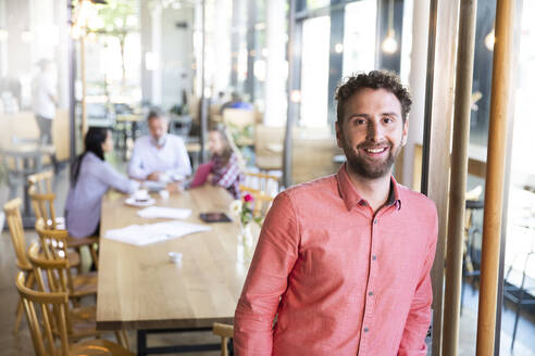 Portrait of casual businessman in a cafe with colleagues having a meeting in background - FKF03682