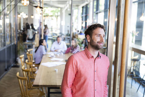 Porträt eines lässigen Geschäftsmannes in einem Café mit Kollegen, die im Hintergrund eine Besprechung abhalten, lizenzfreies Stockfoto