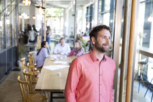 Portrait of casual businessman in a cafe with colleagues having a meeting in background - FKF03683