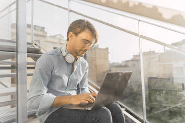 Casual businessman sitting on stairs using laptop - AFVF03983