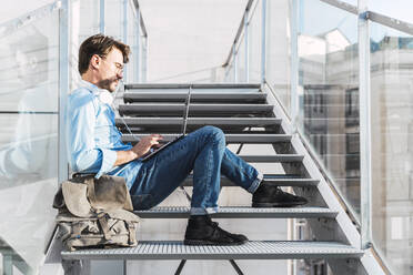 Lässiger Geschäftsmann, der auf einer Treppe sitzt und einen Laptop benutzt - AFVF03986