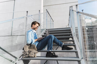 Casual businessman sitting on stairs using laptop - AFVF03987