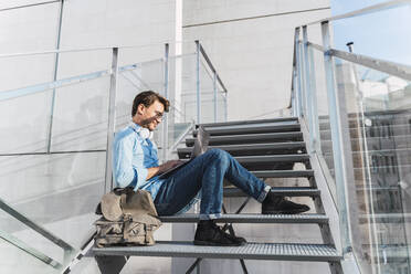 Lässiger Geschäftsmann, der auf einer Treppe sitzt und einen Laptop benutzt - AFVF03987