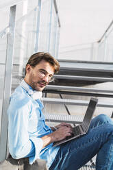 Porträt eines lässigen Geschäftsmannes, der auf einer Treppe sitzt und einen Laptop benutzt - AFVF03989