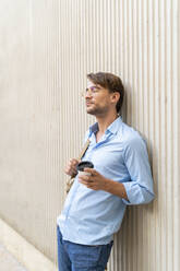 Casual businessman with takeaway coffee leaning against a wall - AFVF03992