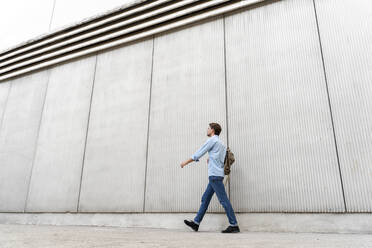 Lässiger Geschäftsmann, der an einer Mauer entlang geht - AFVF03996