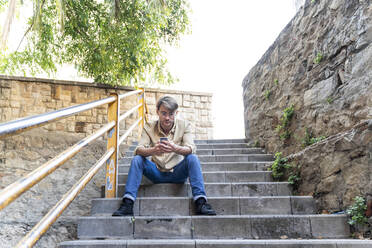 Man sitting on outdoor stairs using cell phone - AFVF03999