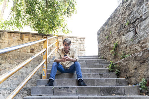 Mann sitzt auf einer Außentreppe und benutzt ein Mobiltelefon - AFVF03999