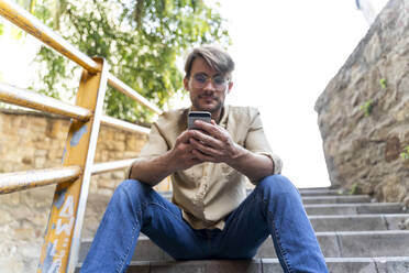 Mann sitzt auf einer Außentreppe und benutzt ein Mobiltelefon - AFVF04000