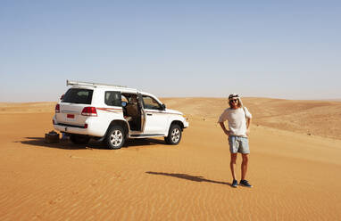 Tourist standing in the desert next to off-road vehicle, Wahiba Sands, Oman - WWF05286