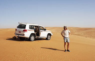 Tourist steht in der Wüste neben einem Geländewagen, Wahiba Sands, Oman - WWF05286