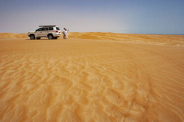 Tourist im Gespräch mit seinem Fahrer in der Wüste neben einem Geländewagen, Wahiba Sands, Oman - WWF05296