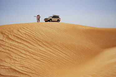Tourist standing on dune next to off-road vehicle with his driver, Wahiba Sands, Oman - WWF05298