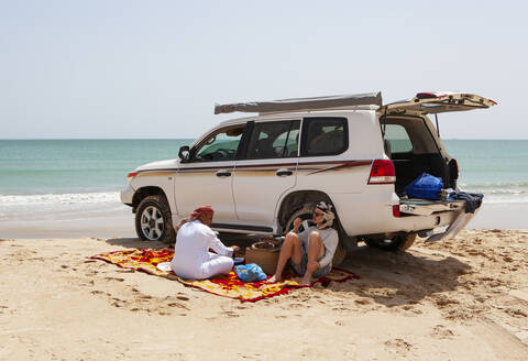 Tourist bei einer Kaffeepause mit seinem einheimischen Fahrer am Indischen Ozean, Oman, lizenzfreies Stockfoto