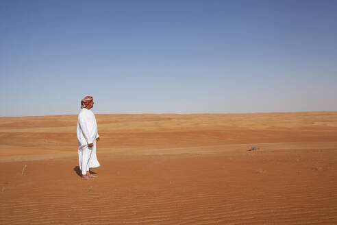 Beduine in Nationaltracht in der Wüste stehend, Rückansicht, Wahiba Sands, Oman - WWF05313