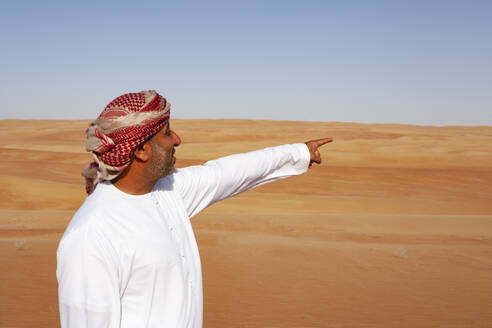 Beduine in Nationaltracht in der Wüste stehend, in die Ferne zeigend, Wahiba Sands, Oman - WWF05314