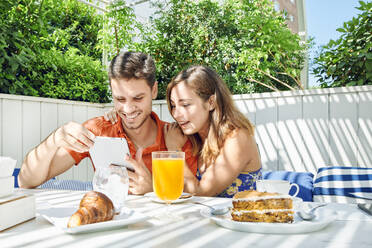 Cheerful young couple using tablet during breakfast - JNDF00109