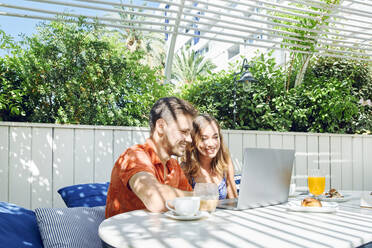 Cheerful young couple using laptop during breakfast - JNDF00113