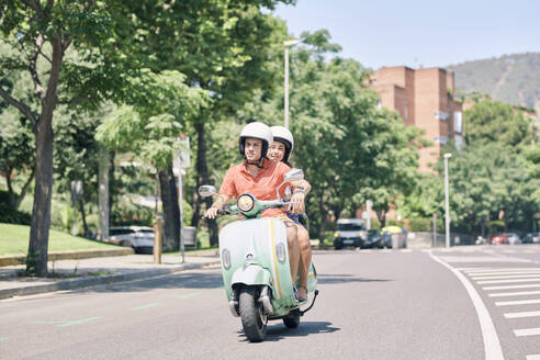Young couple riding vintage motor scooter on urban road - JNDF00122