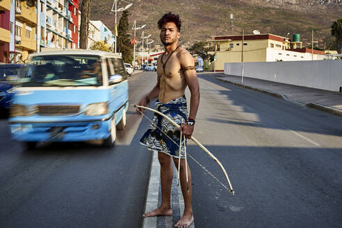 Tribal man with his traditional arch and arrows in the middle of the city with cars passing by, Lubango, Angola - VEGF00762