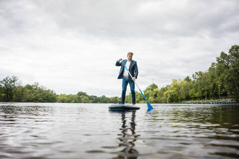 Geschäftsmann beim Stand Up Paddling auf einem See, lizenzfreies Stockfoto