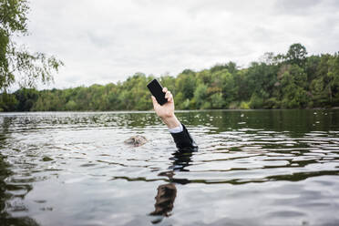 Businessman's hand holding cell phone inside a lake - JOSF03784