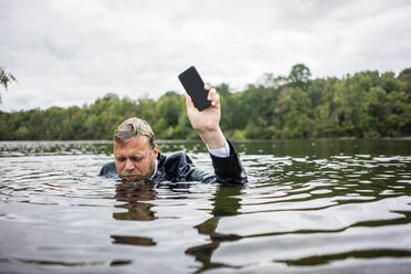 Businessman holding cell phone inside a lake - JOSF03787