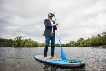 Geschäftsmann mit VR-Brille auf SUP-Board auf einem See - JOSF03792