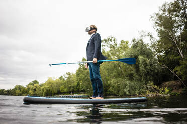 Geschäftsmann mit VR-Brille auf SUP-Board auf einem See - JOSF03794