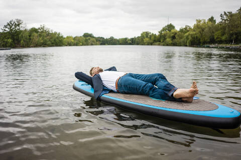 Geschäftsmann liegend auf SUP-Board auf einem See, lizenzfreies Stockfoto