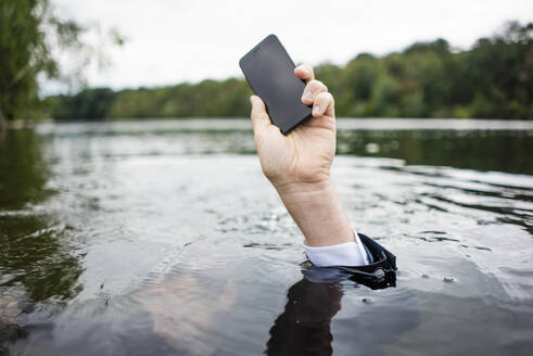 Businessman's hand holding cell phone inside a lake - JOSF03799