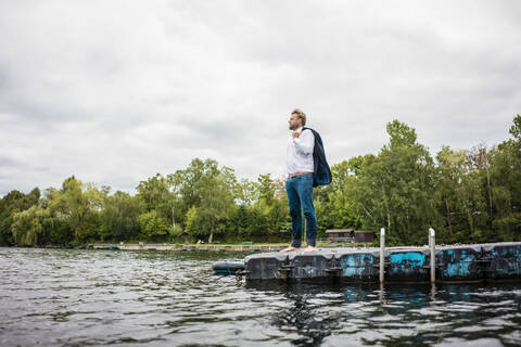Geschäftsmann steht auf einem Schwimmer und schaut auf einen See hinaus, lizenzfreies Stockfoto