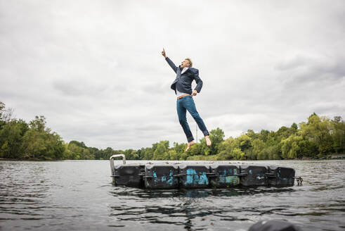 Geschäftsmann springt auf Plattform in einem See - JOSF03802