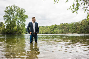 Businessman standing in a lake looking out - JOSF03808