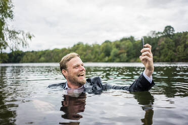 Mad businessman holding cell phone inside a lake - JOSF03818