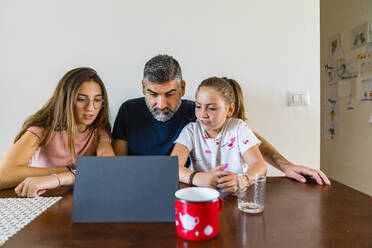 Vater mit zwei Töchtern schaut auf ein Tablet auf einem Holztisch zu Hause - MGIF00703