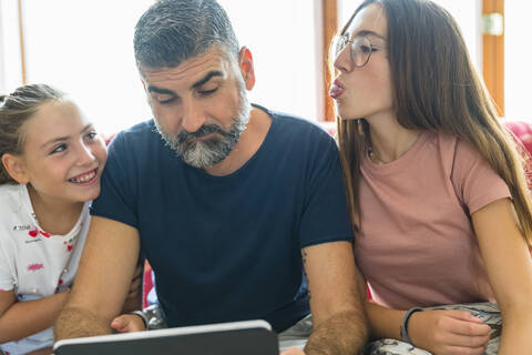 Vater mit zwei Töchtern, die zu Hause auf der Couch auf ein Tablet schauen, lizenzfreies Stockfoto