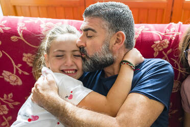 Vater umarmt seine Tochter auf der Couch zu Hause - MGIF00707