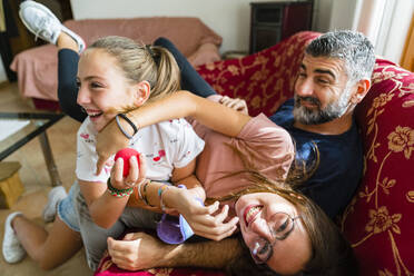 Vater mit zwei verspielten Töchtern auf der Couch zu Hause - MGIF00710
