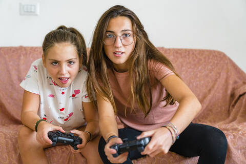 Sisters playing video game on couch at home stock photo