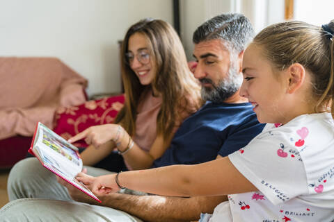 Vater mit zwei Töchtern betrachtet Fotoalbum auf der Couch zu Hause, lizenzfreies Stockfoto
