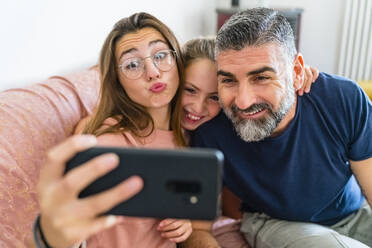 Happy father with two daughters taking selfie on couch at home - MGIF00718