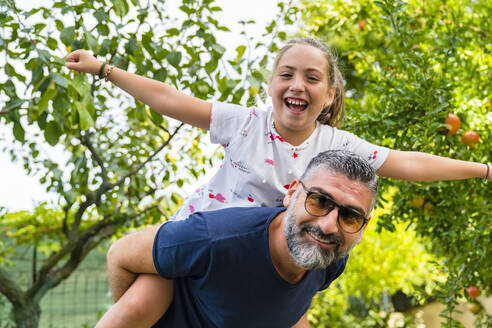 Father carrying happy daughter piggyback in garden - MGIF00720