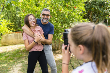 Girl taking a picture of happy father with daughter in garden - MGIF00723