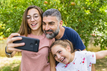 Glücklicher Vater mit zwei Töchtern macht Selfie im Garten - MGIF00728